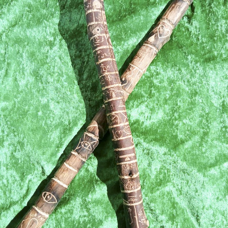 Two carved story sticks bound with twine, crossed on green velvet