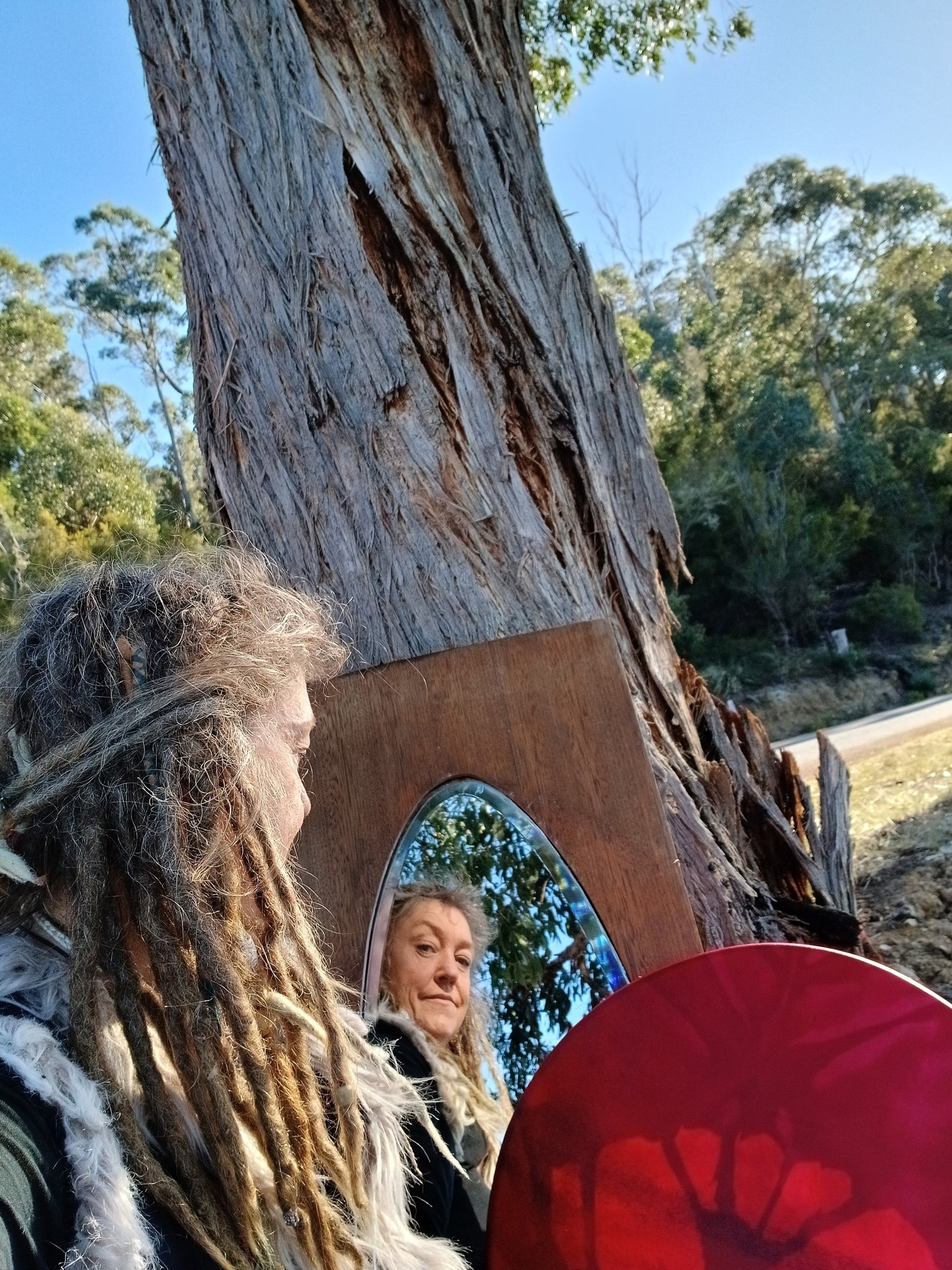 Teula Wylde standing beside an ancient tree and ceremonial mirror